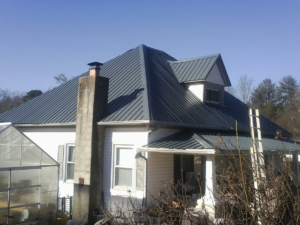 Dark blue standing seam metal roof on a white farmhouse with dormer — Slate & Tile Roof Repair by Roofing Brothers in North Fork