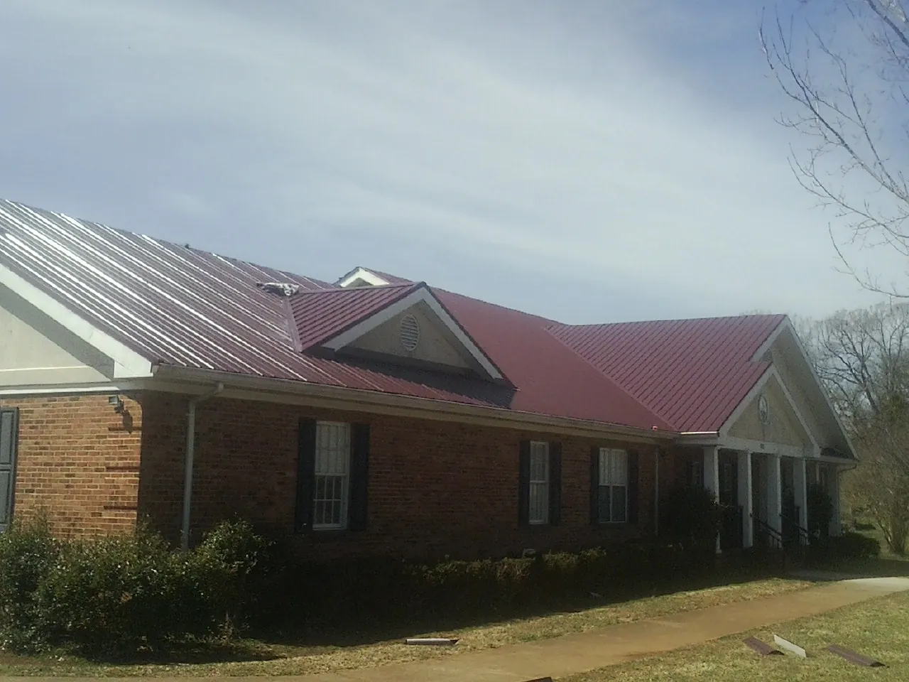 Red metal roof with gabled entries on a long brick building, from a Hail Damage Roof Repair job in North Fork