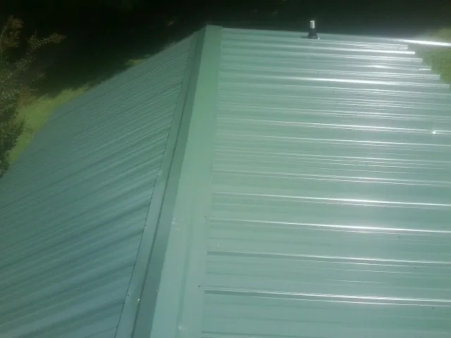 New green metal panels meeting at the ridge of a roof — Flat Roof Repair work by our crew in North Fork