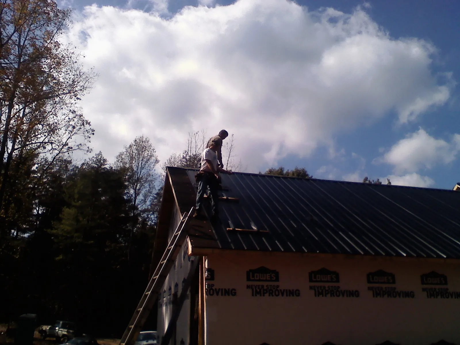 Roofer fastening dark metal panels high against a cloudy sky, from a Roof Inspection job in North Fork