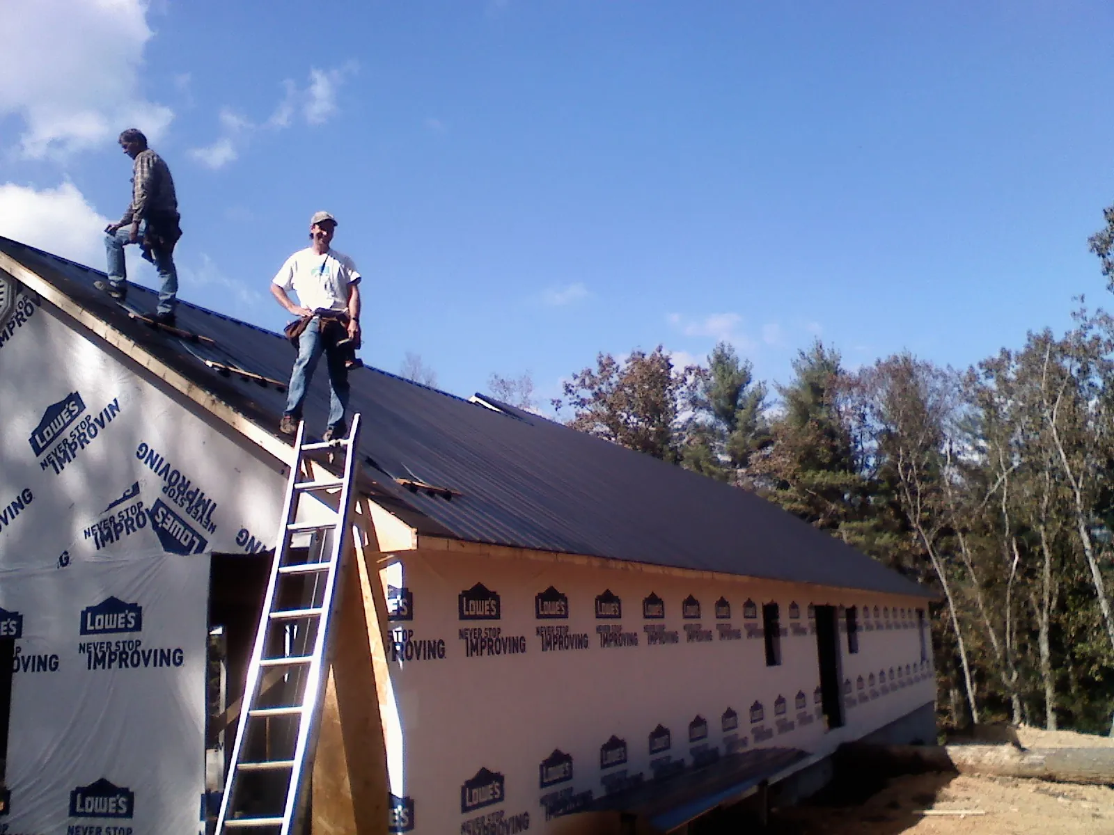 Two roofers standing on a long dark metal roof over a wrapped building in North Fork