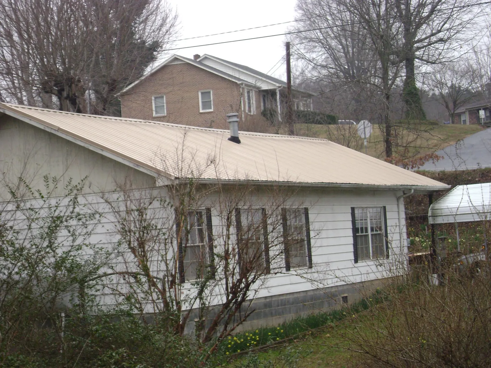 Tan metal roof on a white sided house set into a hillside — Commercial Roofing by Roofing Brothers in North Fork